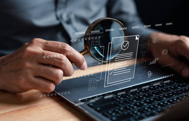 Person holding a magnifying glass over a laptop screen with a document icon