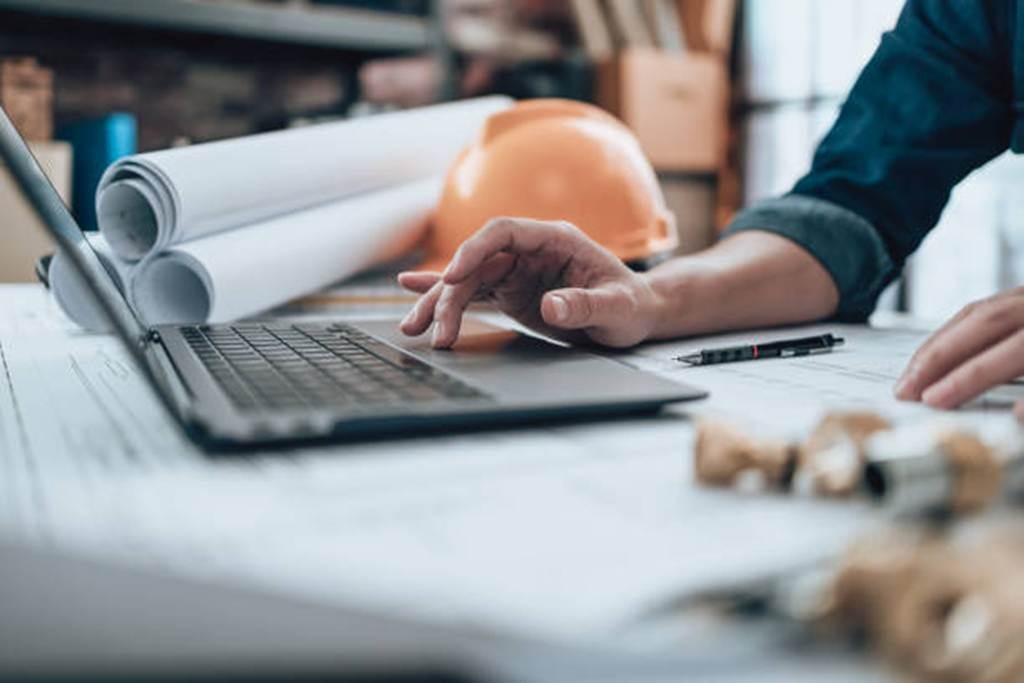Construction office desk with laptop, plans, and hard hat