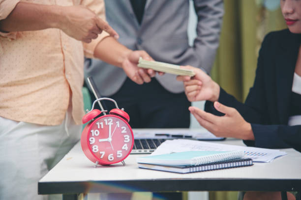 Clock on desk with people exchanging money