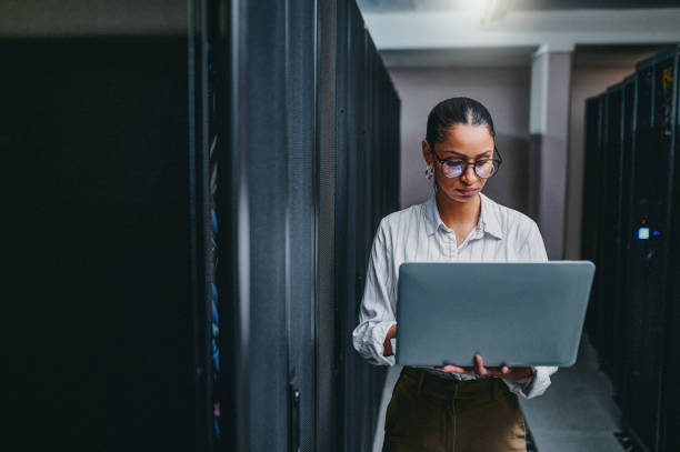 Woman standing in a server room holding a laptop