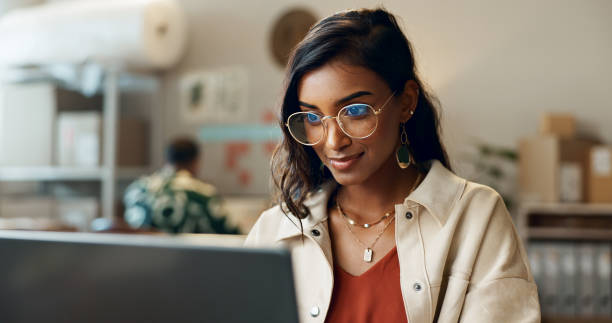 Woman with glasses looking at a laptop in an office setting