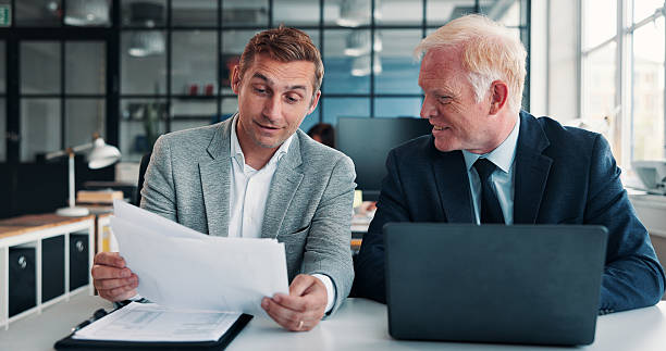 Two men looking at documents and a laptop
