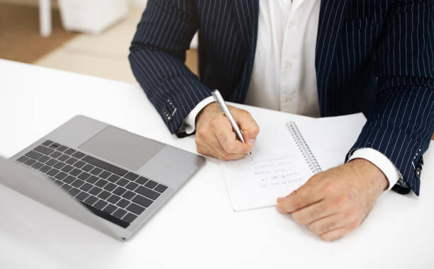 Employee writing timekeeping SOP on a notebook with a laptop