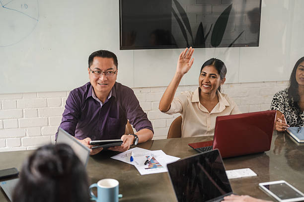 People in a meeting room, one raising hand