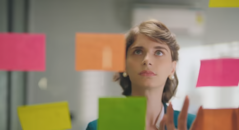 Woman looking at colorful sticky notes on a glass wall