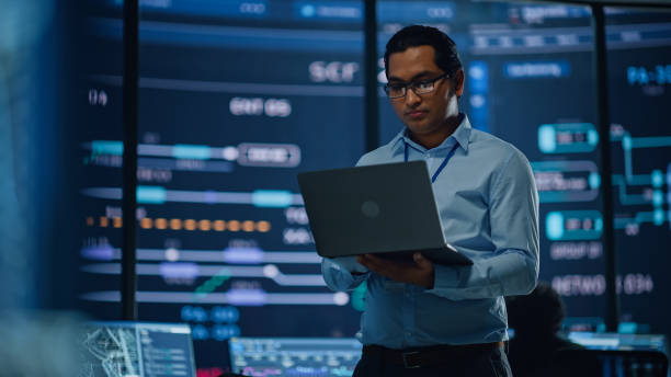 Man with glasses holding a laptop in a server room