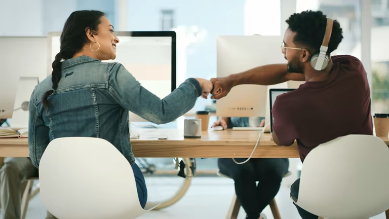 Two people fist-bumping at a desk