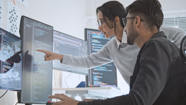 Software team reviewing payroll and HR integration data on multiple monitors