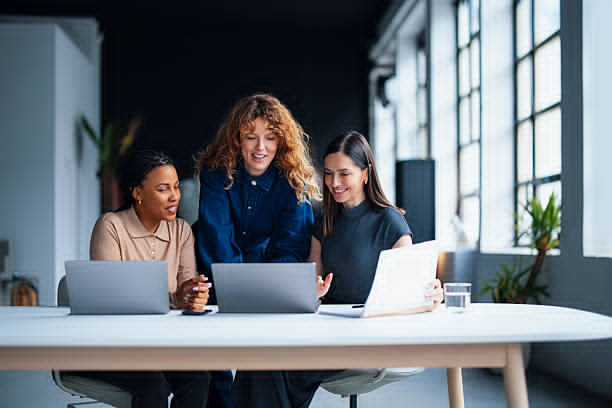 Three women sitting at a desk with laptops