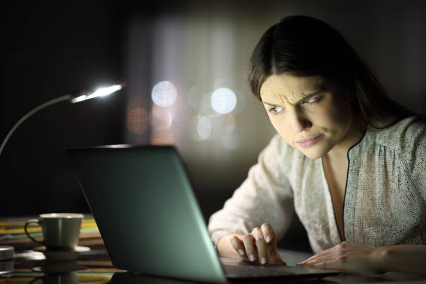 Woman looking suspiciously at laptop in the dark
