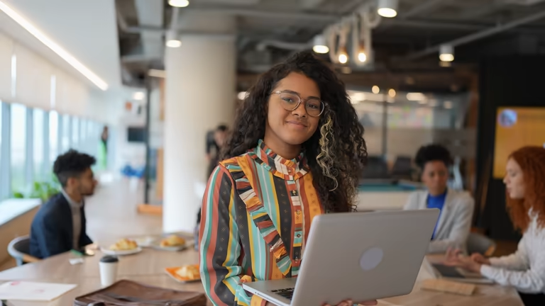 Smiling employee using a laptop with colleagues in the background