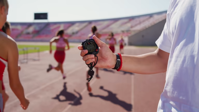 Hand holding a stopwatch with runners on a track