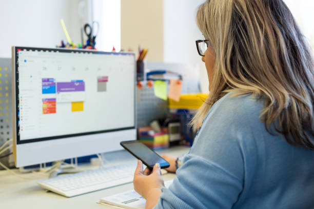 Woman at computer looking at phone