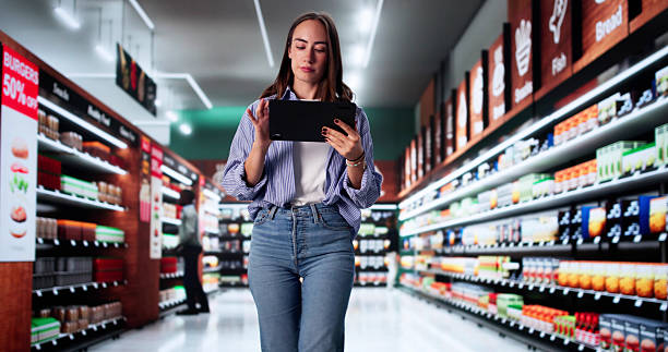 Woman standing in a grocery store aisle looking at a tablet