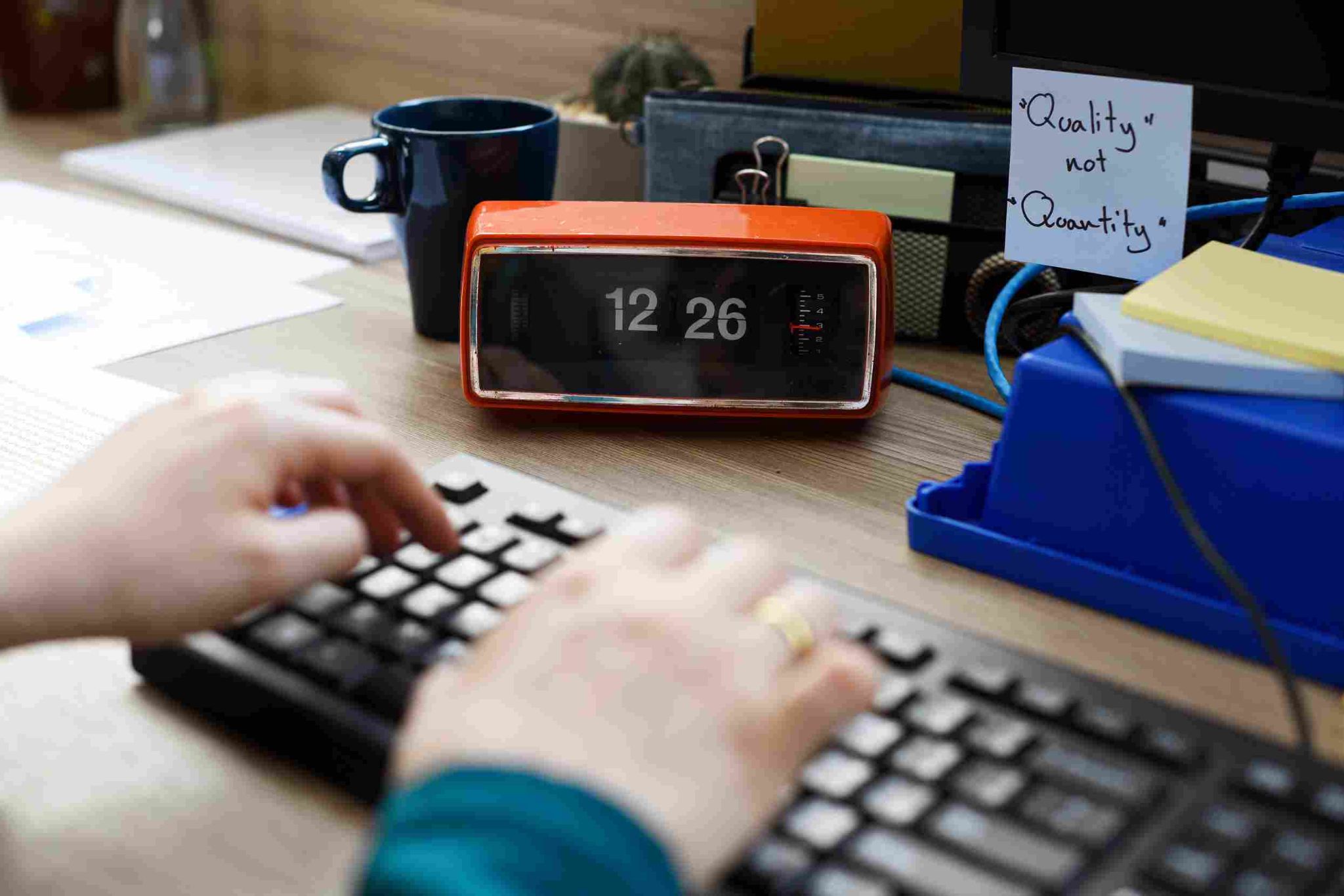 Person typing on a keyboard with a digital clock and sticky notes