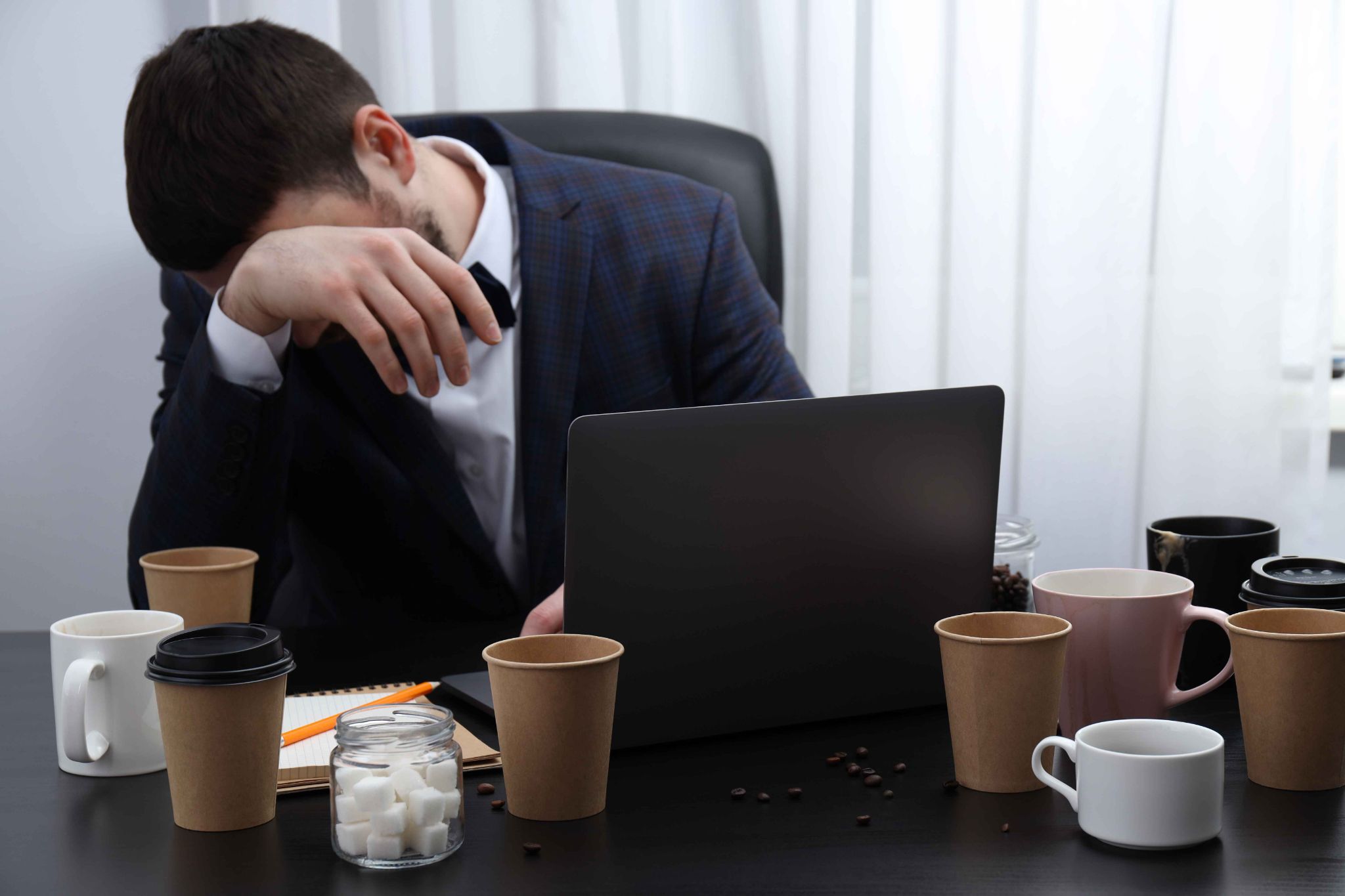 Exhausted employee resting head on hand surrounded by coffee cups