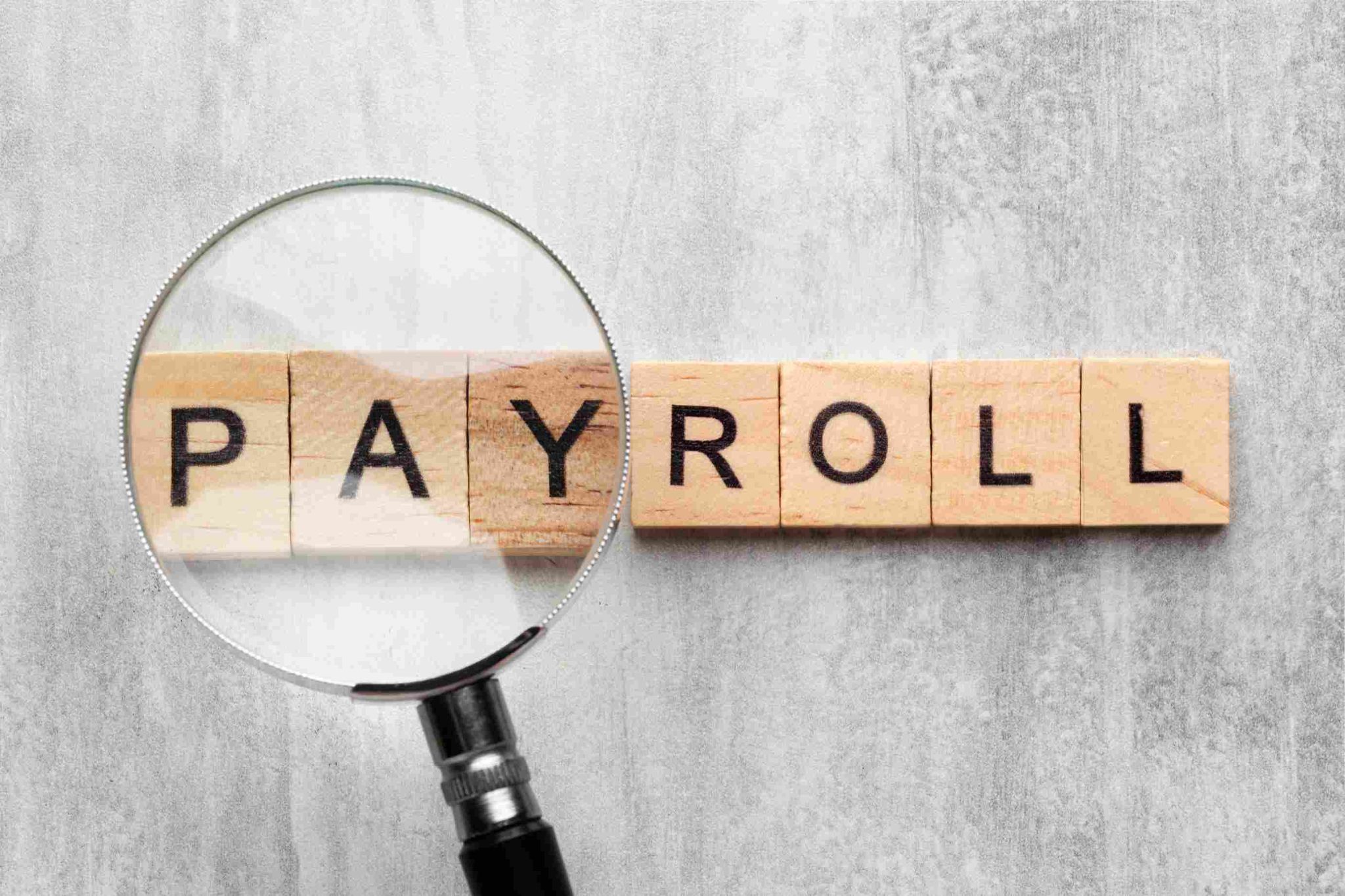 Wooden blocks spelling PAYROLL with a magnifying glass