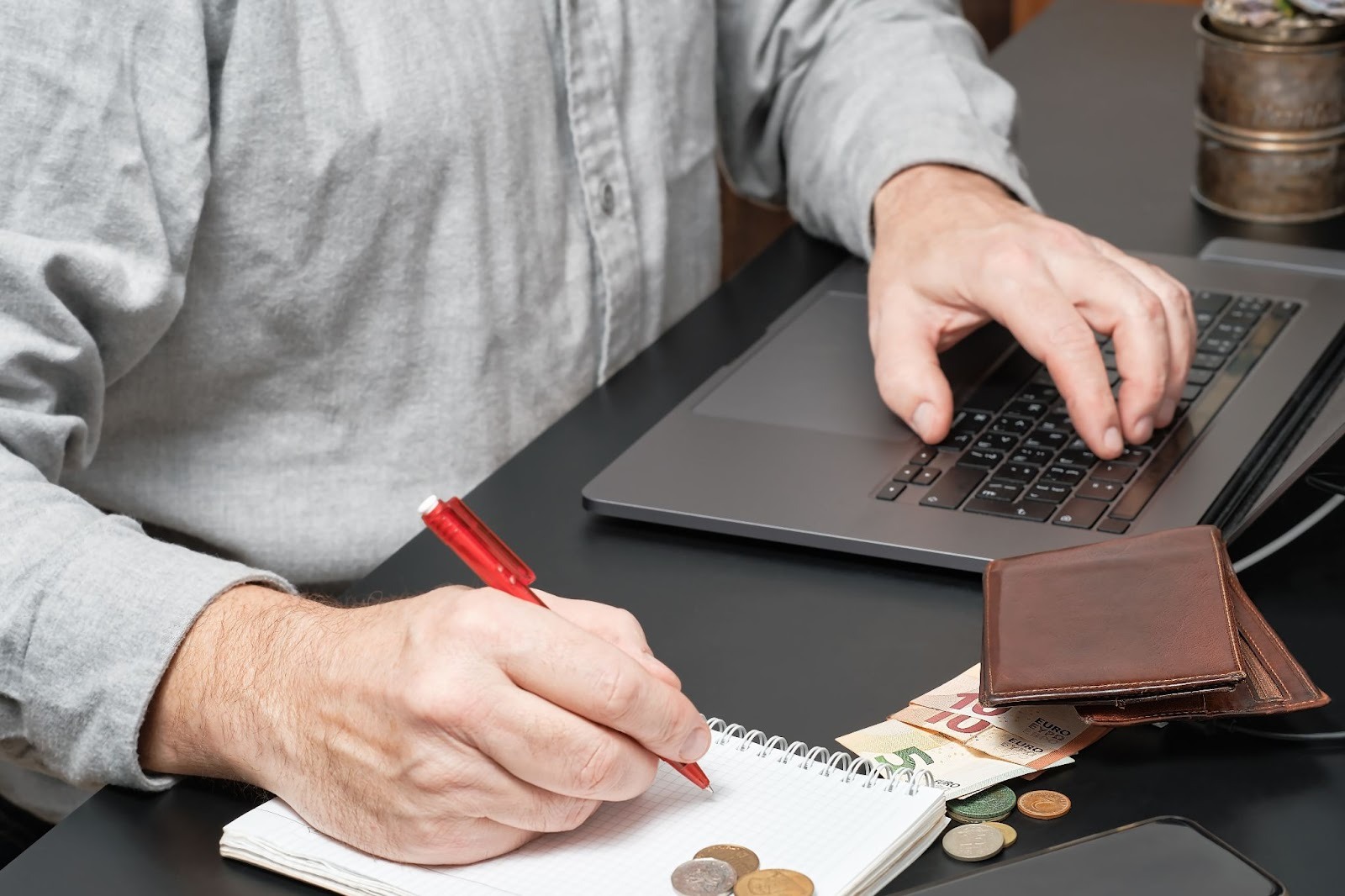 Person calculating wages on a notepad with a laptop and money nearby