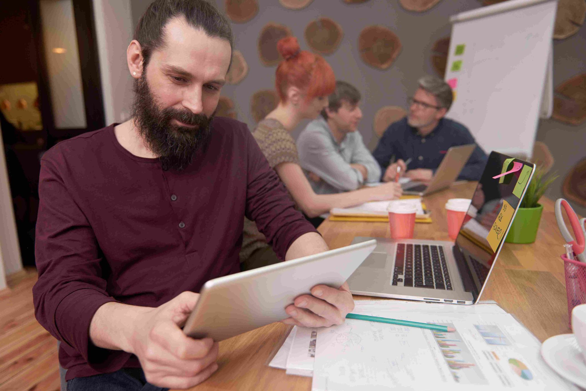 Man with beard looking at tablet with colleagues in background
