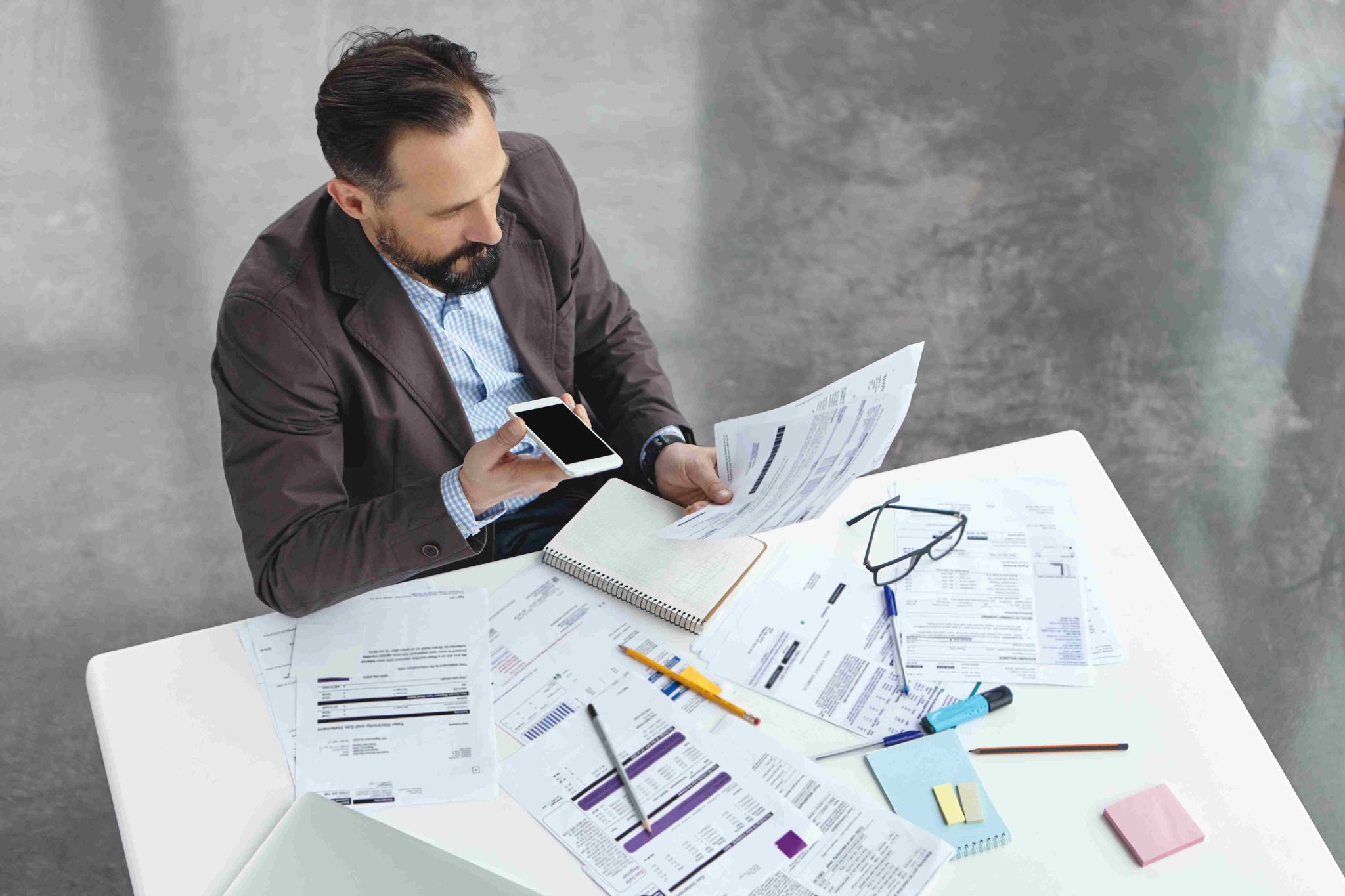 Construction worker looking at phone with papers on desk