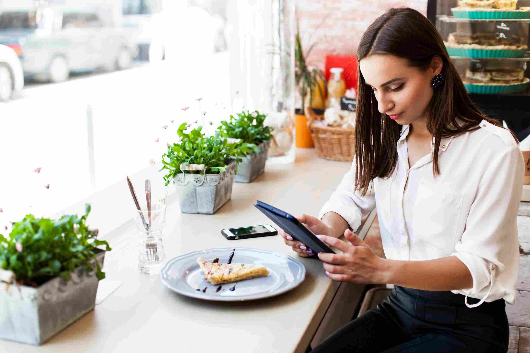 Woman in a white shirt looking at a tablet in a cafe setting