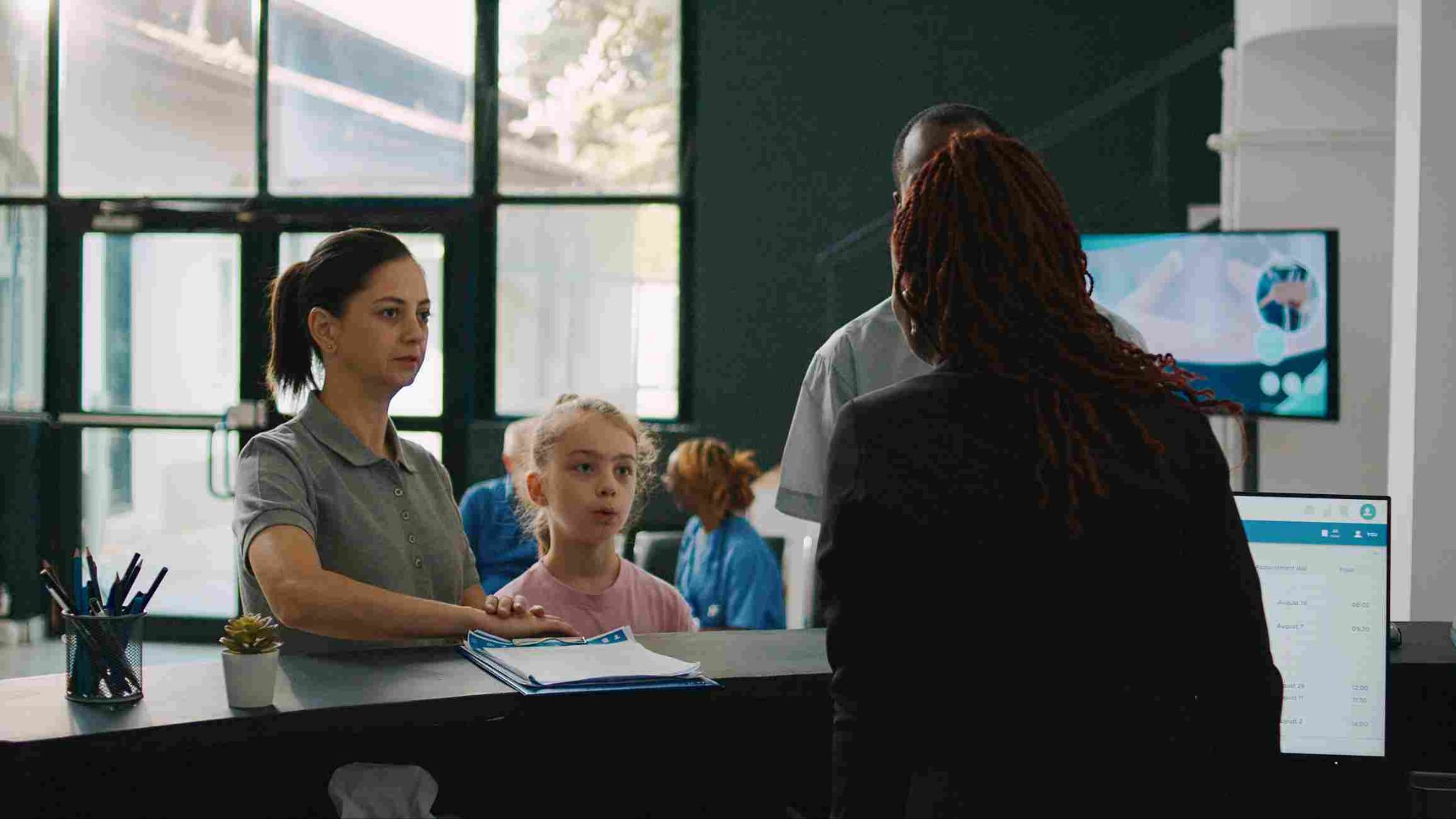Woman at a reception desk talking to a child and another woman