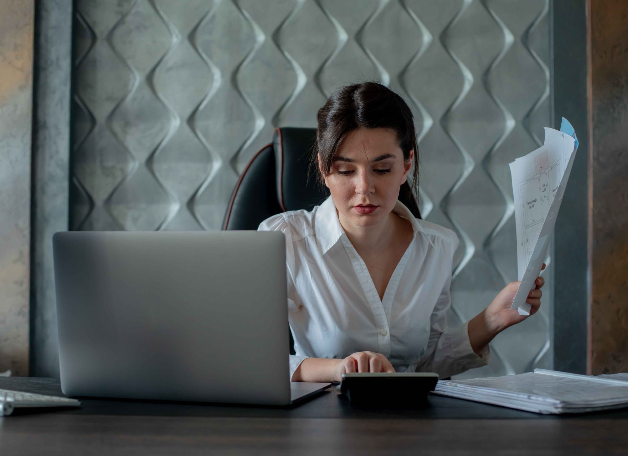 Business professional reviewing documents and payroll calculations on a laptop
