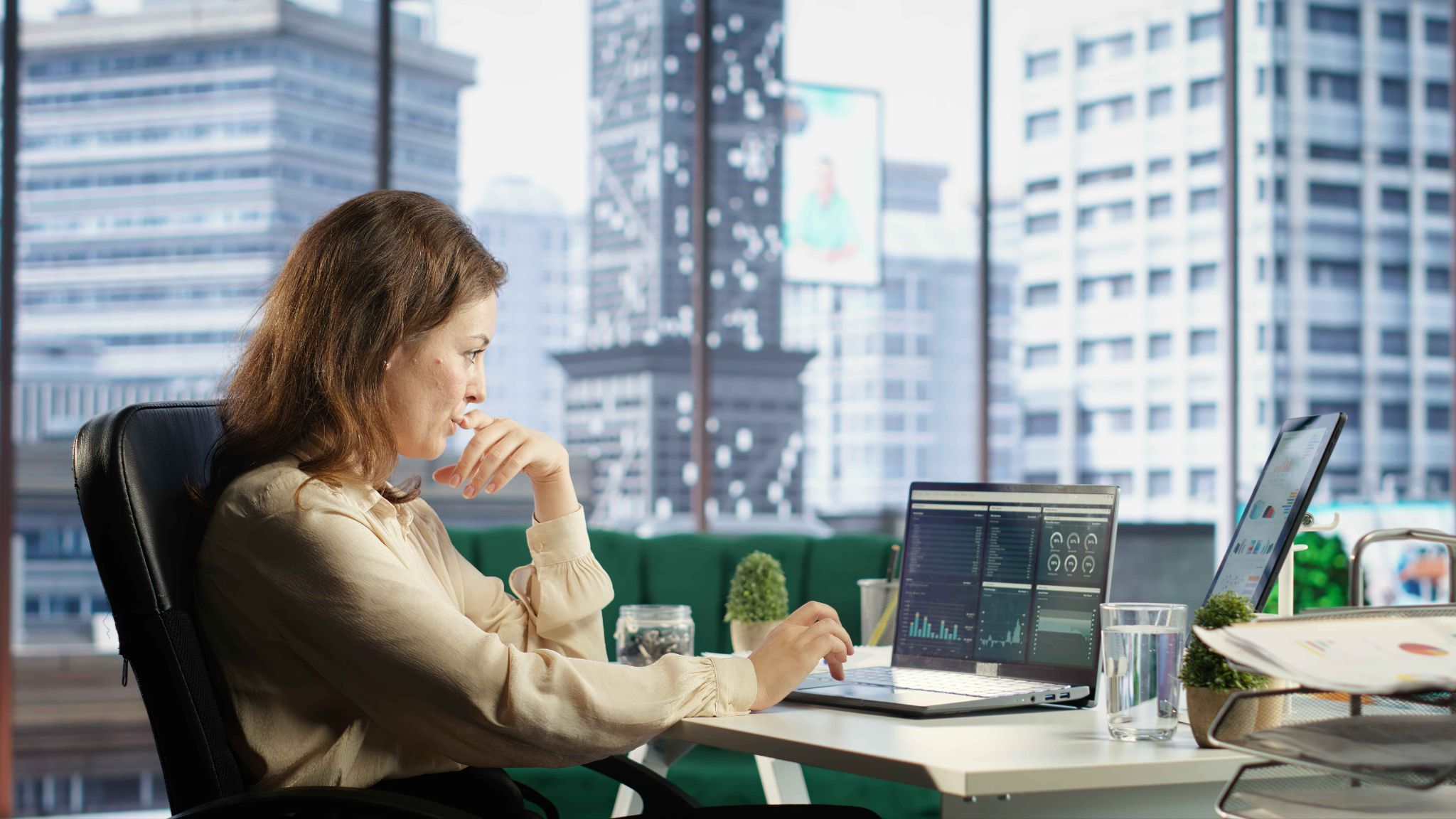 Employee using a laptop in an office with city buildings outside