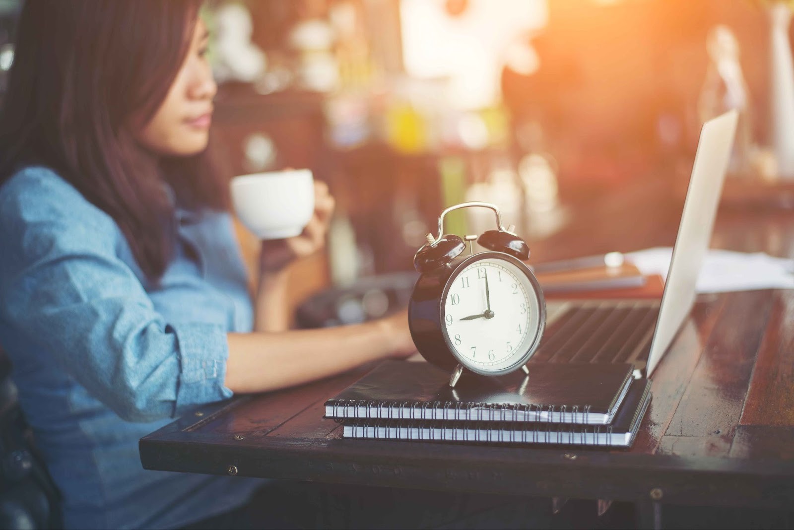 Woman sitting at desk with laptop and alarm clock