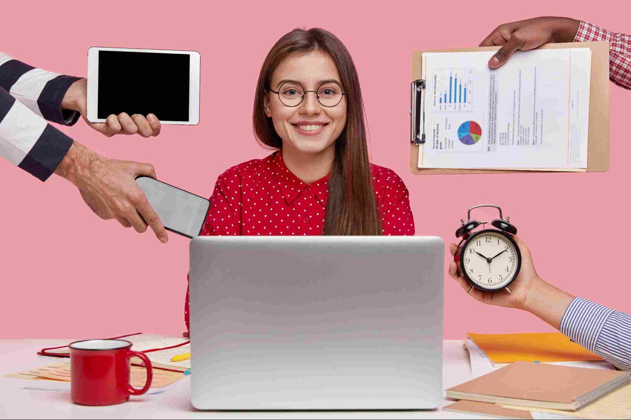 Woman smiling with a laptop, clock, mug, and hands holding a tablet and clipboard