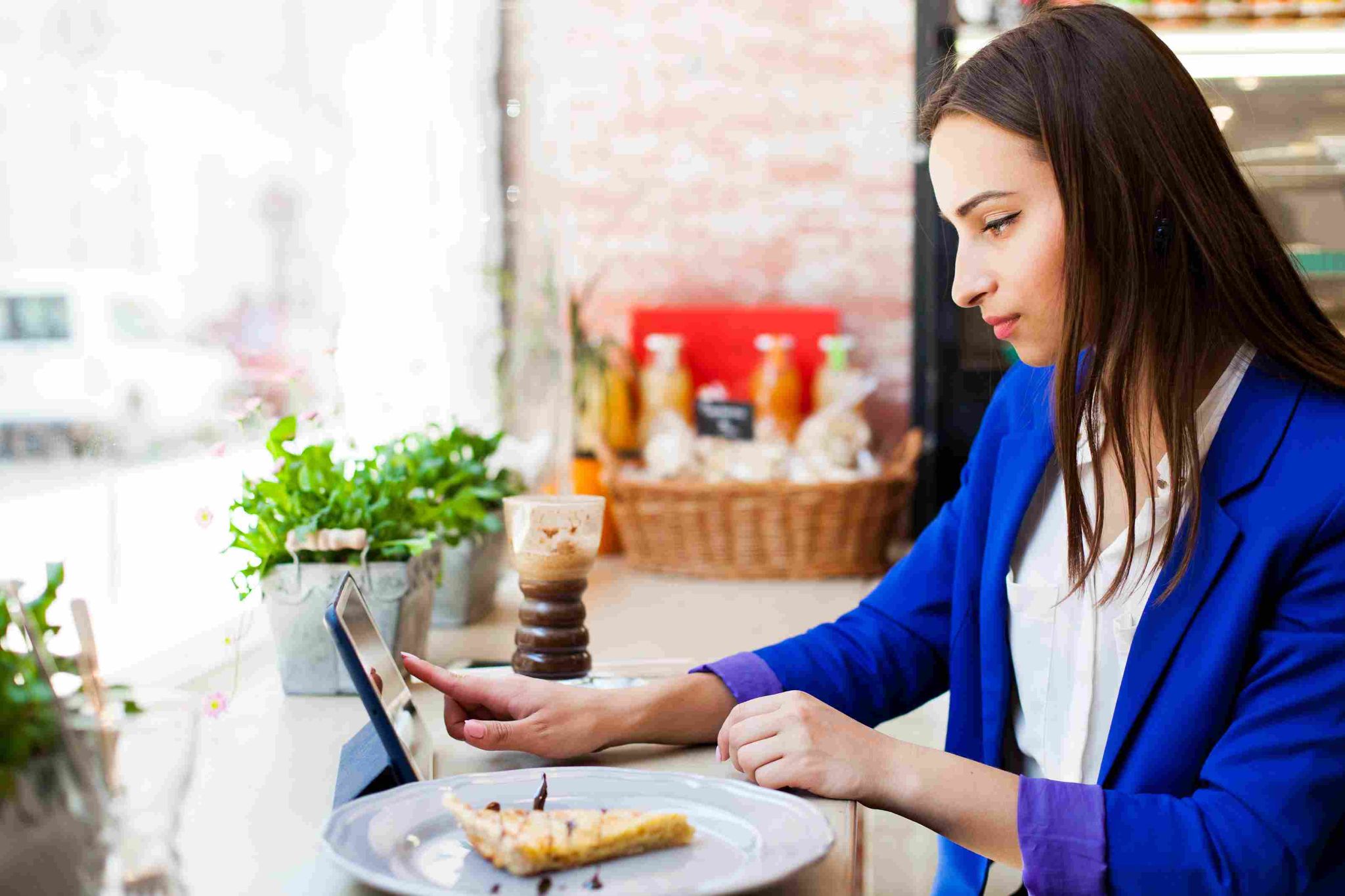 Woman in a blue jacket looking at a tablet while eating a slice of pie
