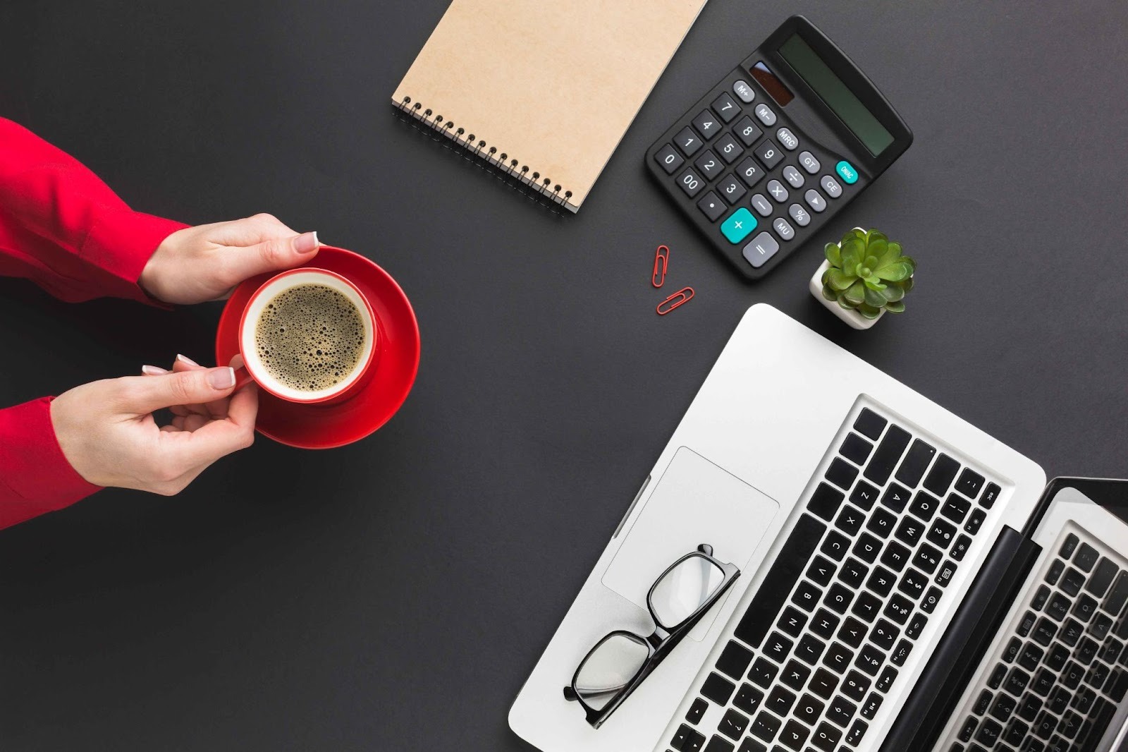 Hands holding coffee cup over a desk with calculator and laptop