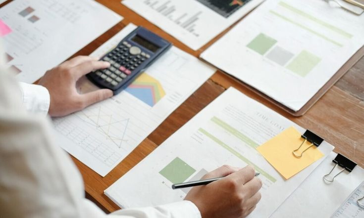 Person using a calculator with financial charts