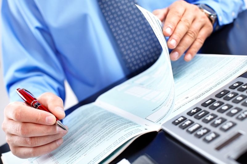 Close-up of a person holding a pen and a document over a calculator