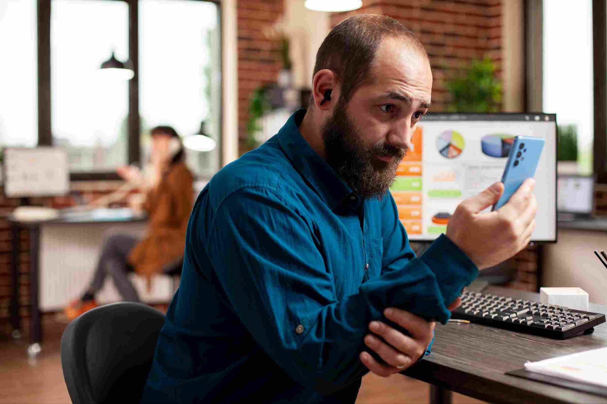 Man with a beard looking at his phone in an office setting