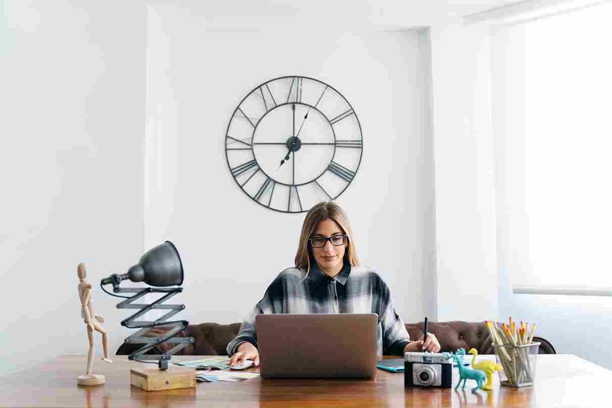 Woman working at a desk with a large wall clock behind her