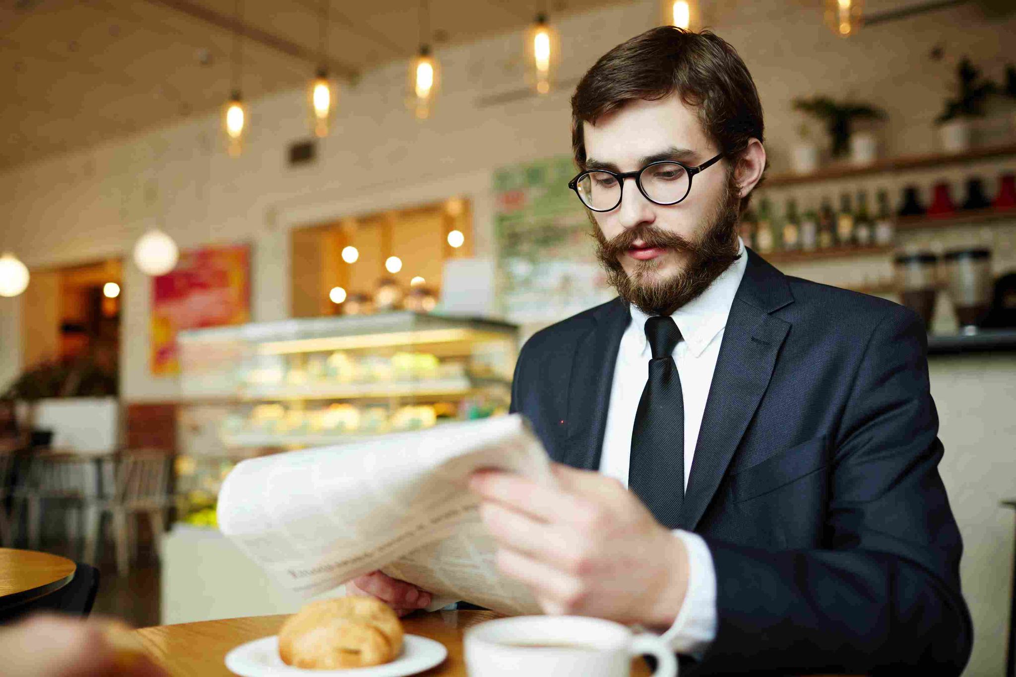 Man with glasses looking at a laptop while drinking coffee