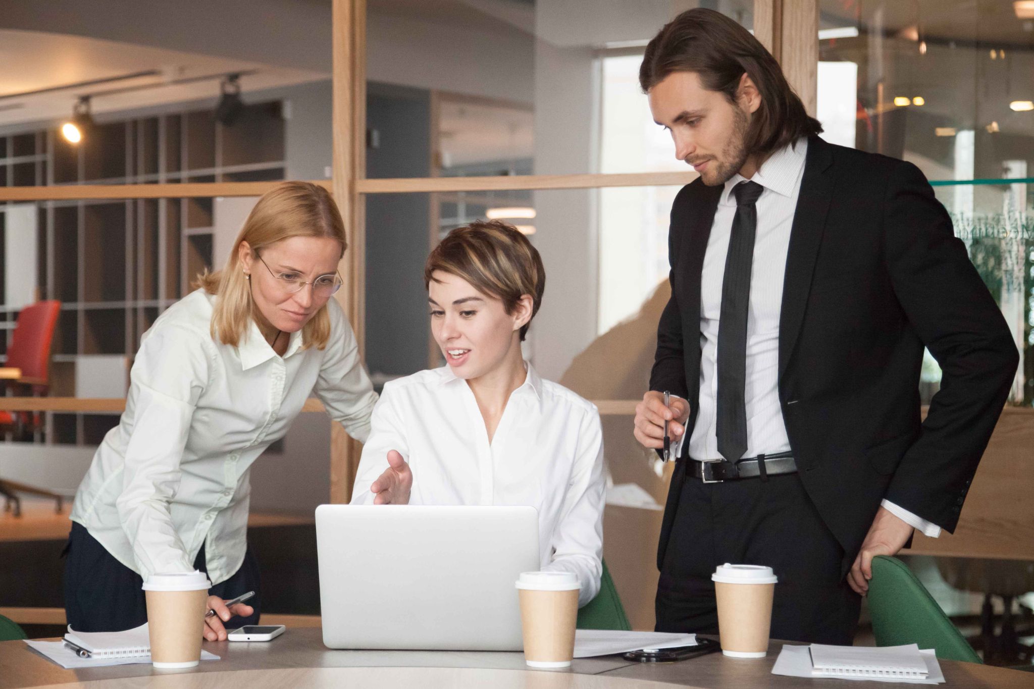Colleagues standing and sitting around a laptop discussing business strategies