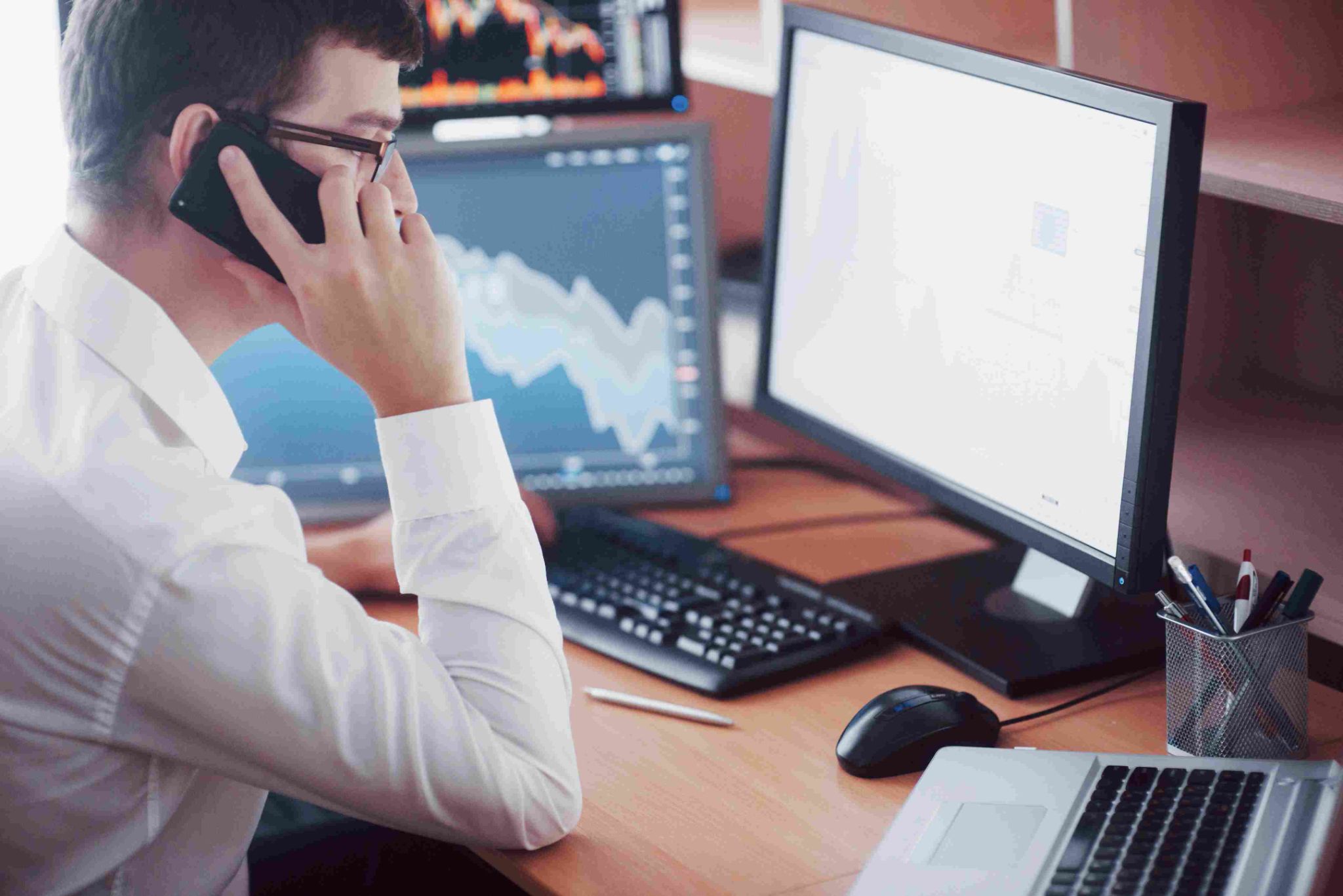 Man on phone looking at multiple monitors with charts