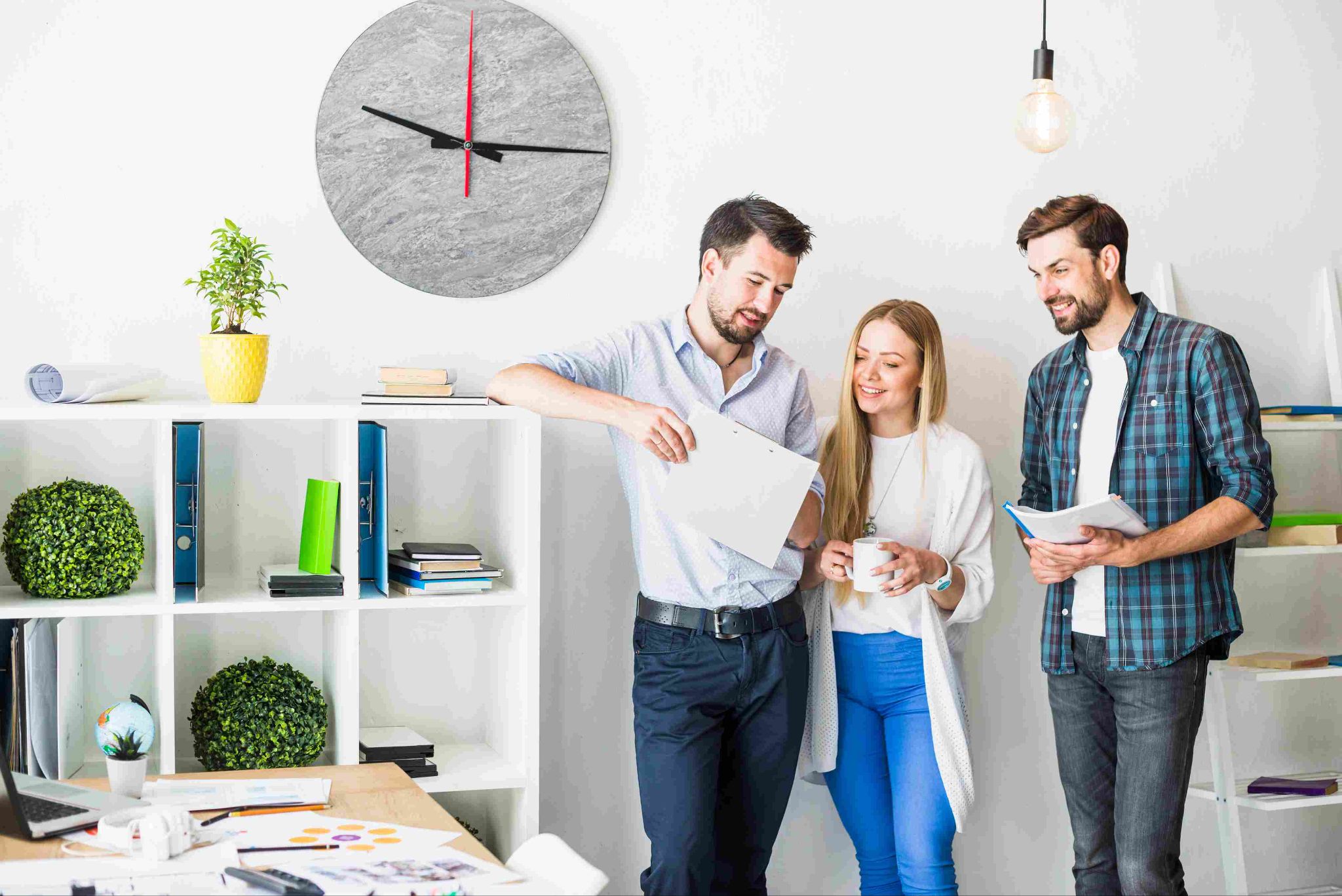 Group of three people looking at papers near a large wall clock