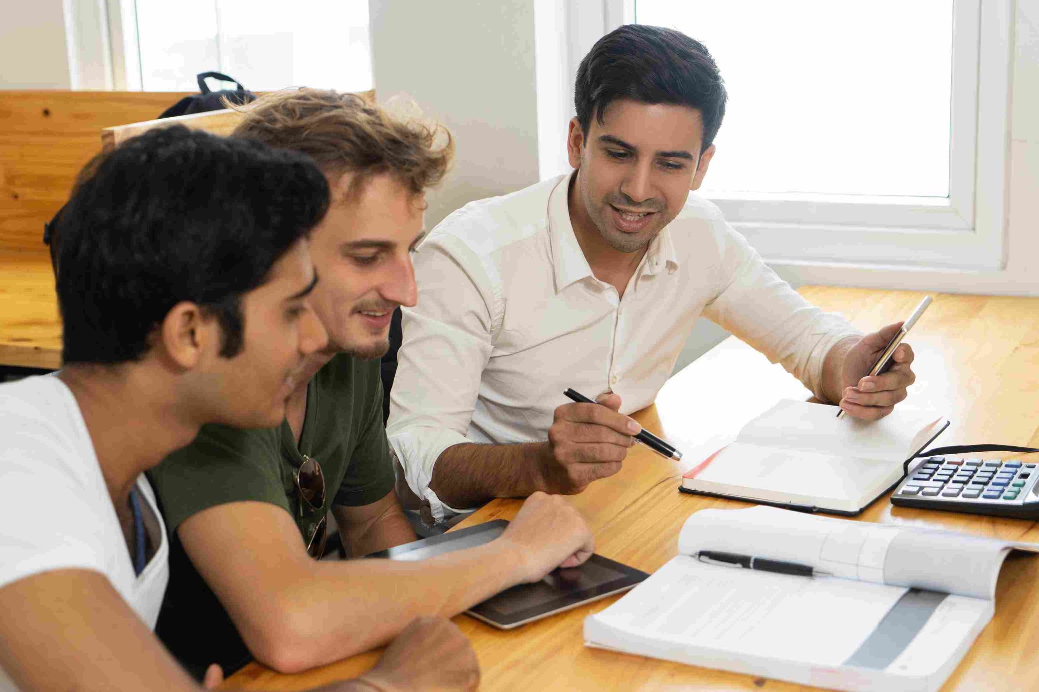 Three men reviewing documents and working on a laptop