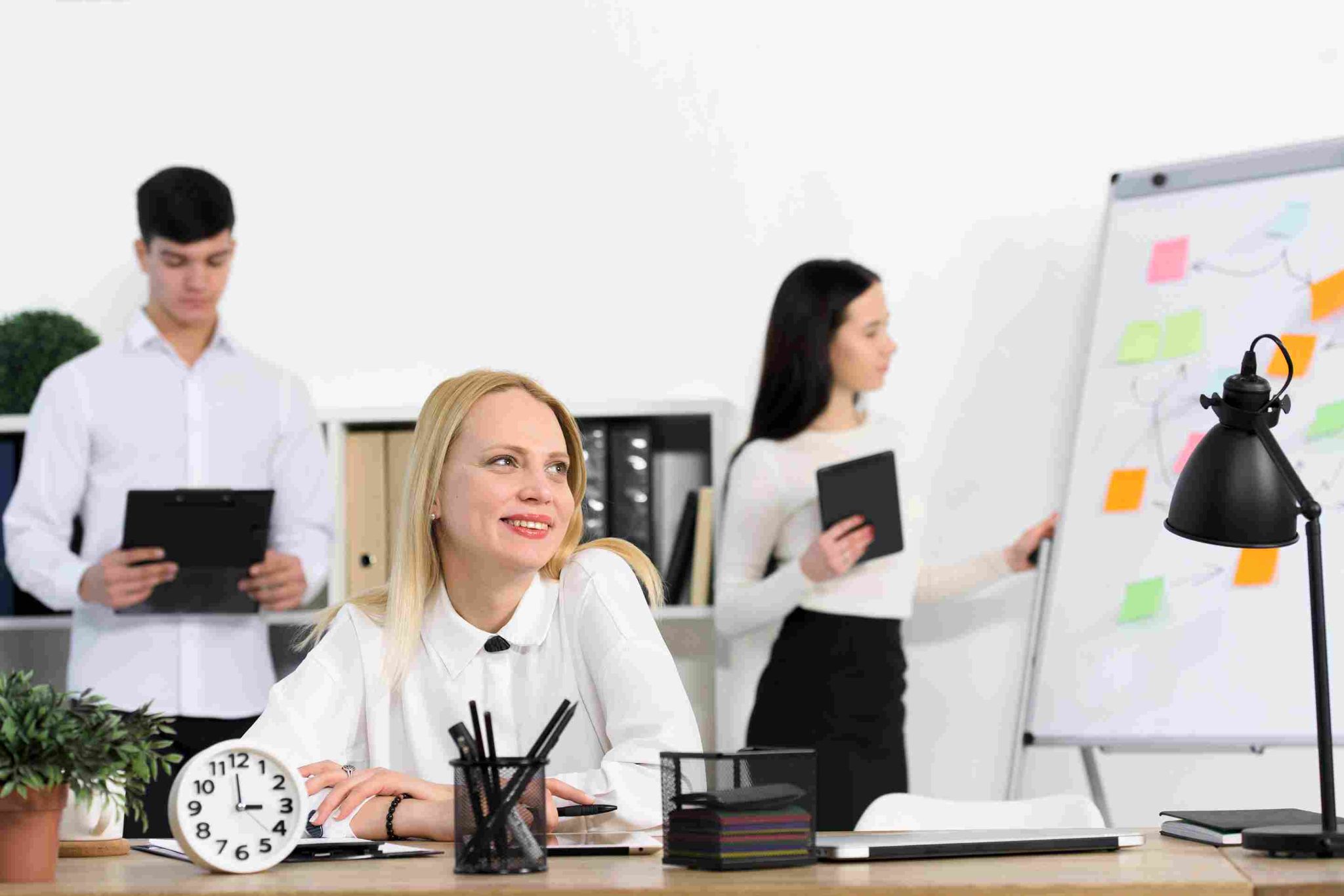 Colleagues working around a desk with a clock in the foreground