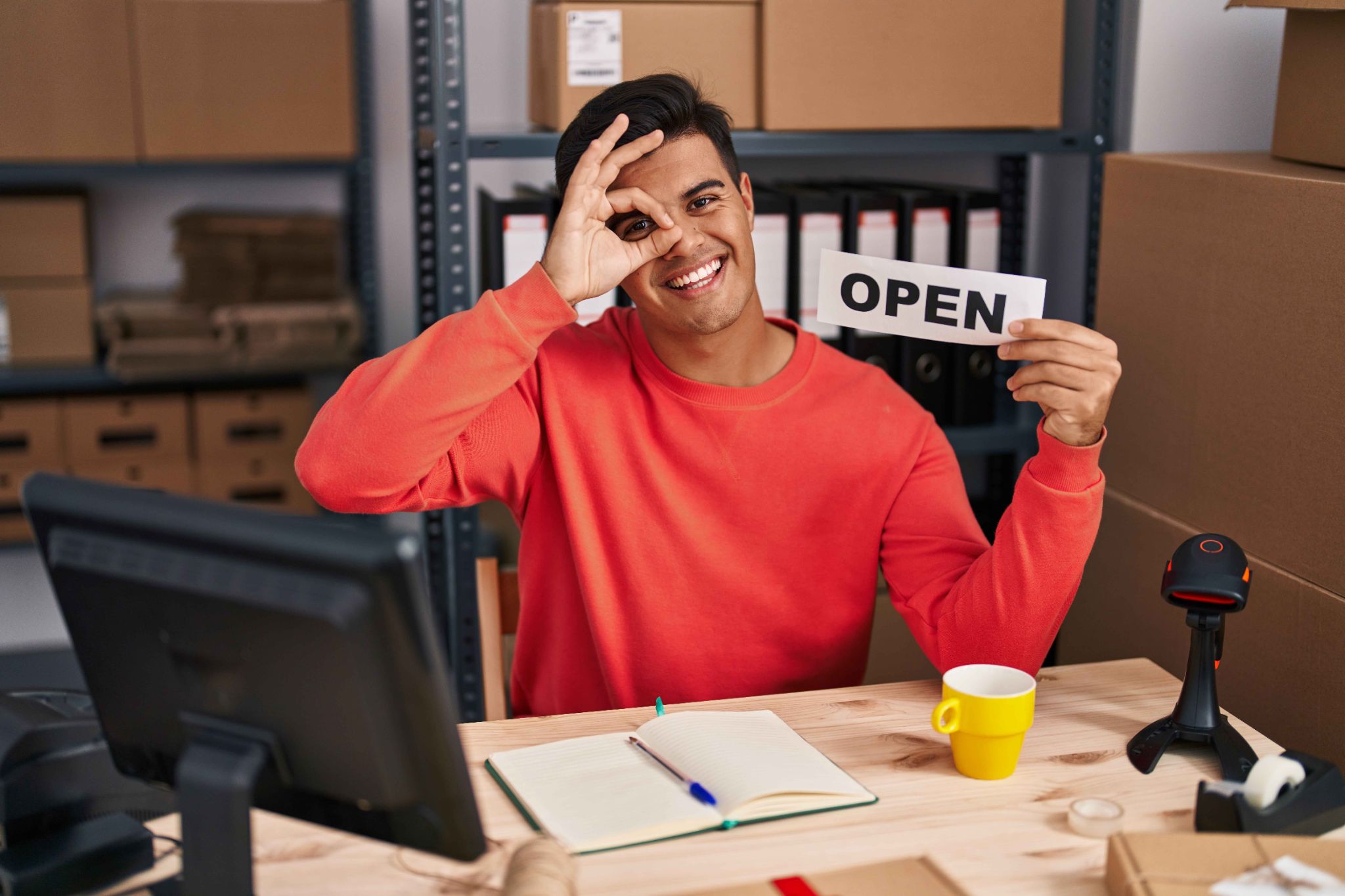 Man making an OK sign over his eye holding an OPEN sign