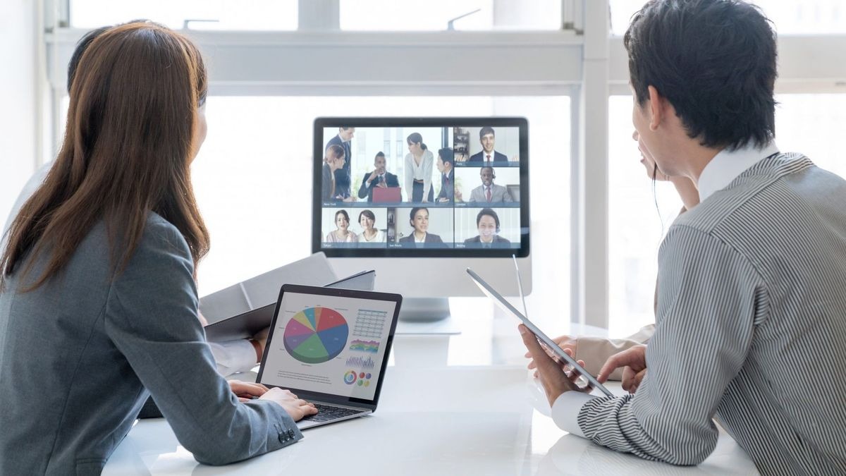 Two people looking at a monitor showing a video call and charts