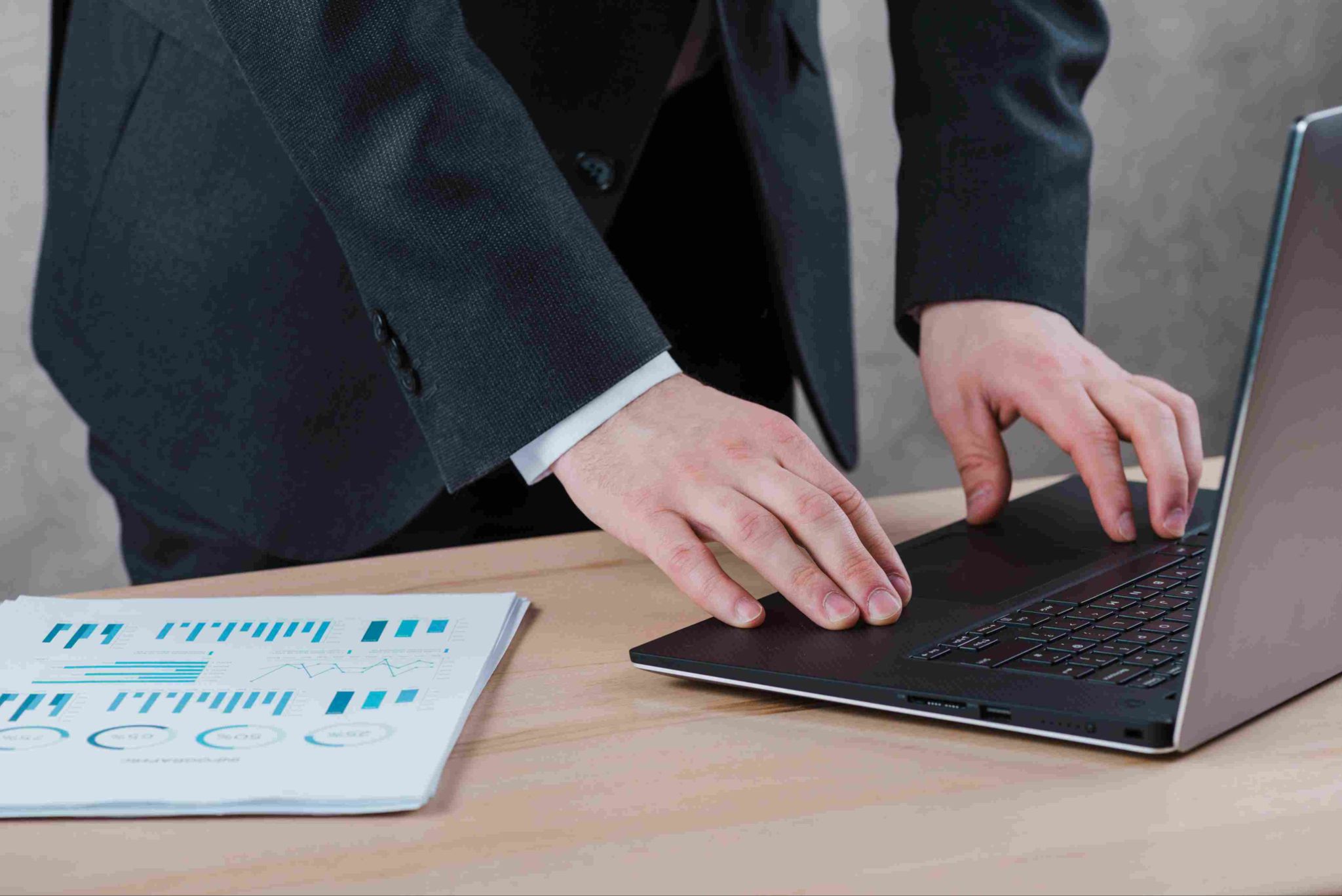 Person typing on a laptop with charts and graphs on the desk