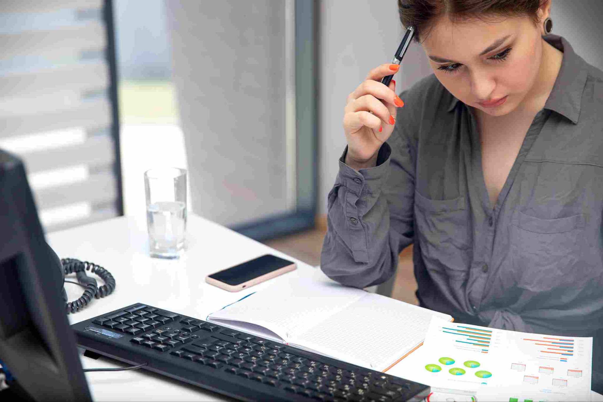 Woman looking thoughtfully at a desk with a phone and notebook