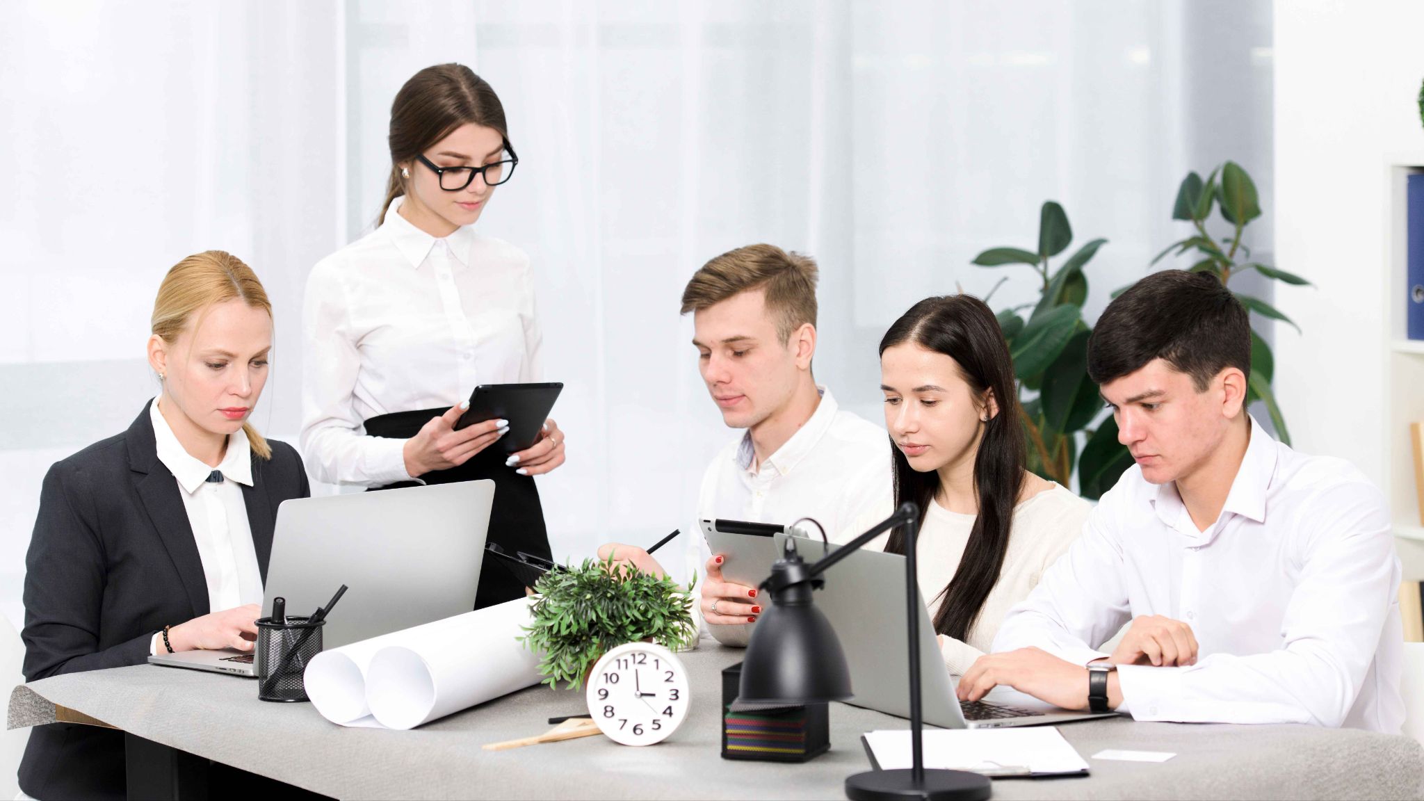 Group of people working at desk with clock and blueprints