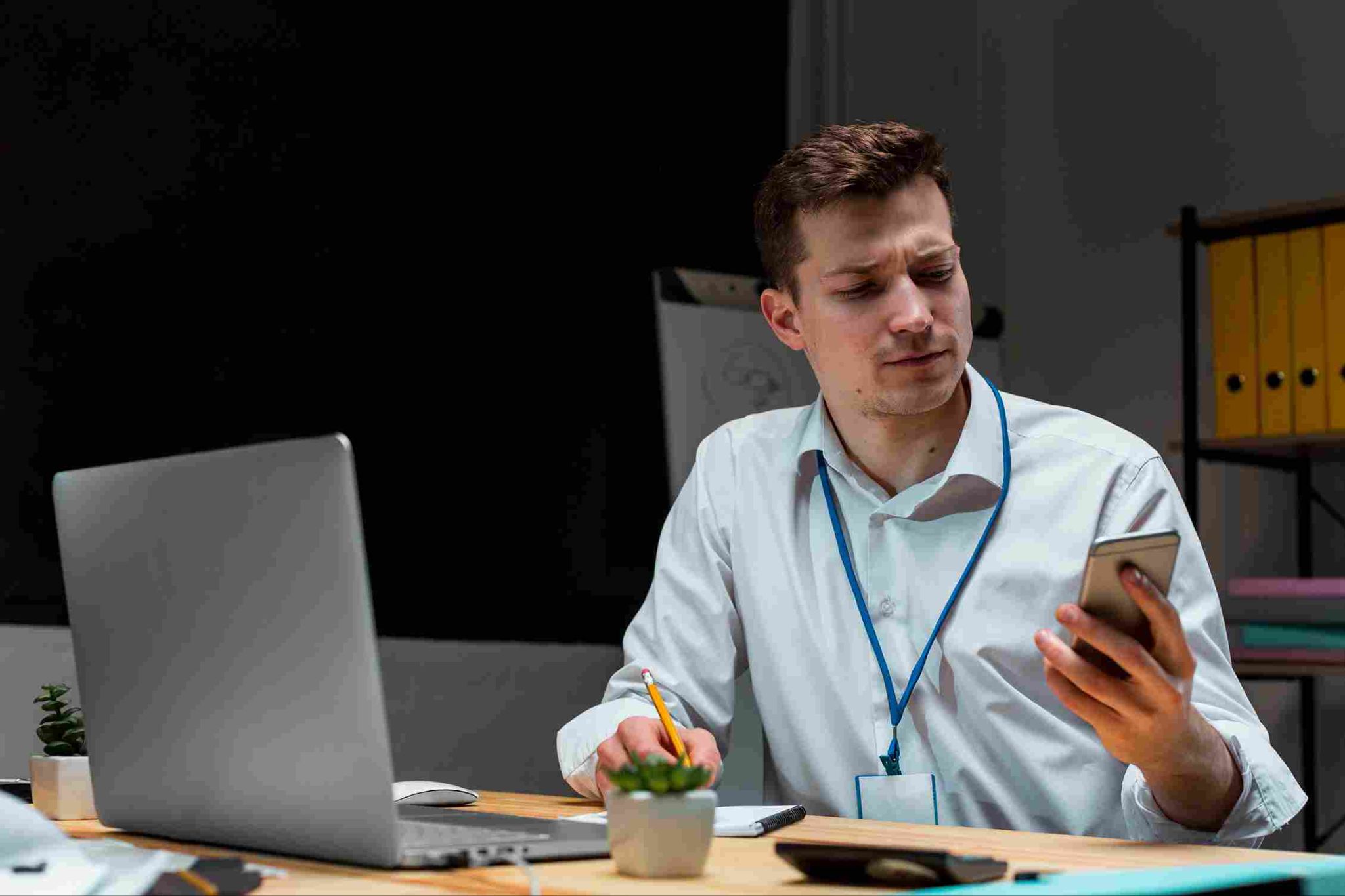 Man at desk looking at his phone and laptop