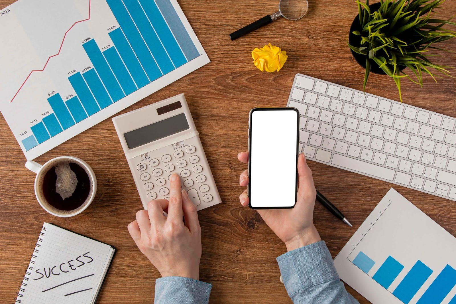 Top-down view of hands using calculator, phone, and charts on a desk
