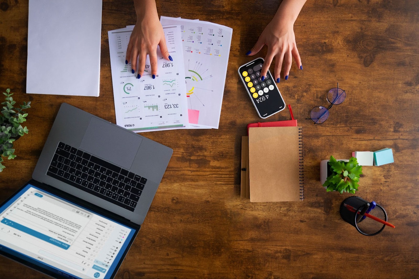 Hands working on documents with a laptop and phone on a wooden desk